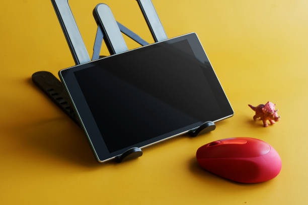 Red modern computer mouse and electronic digital tablet on a stand. Yellow background. The concept of using a wireless computer mouse with mobile gadgets. Electronics concept for children