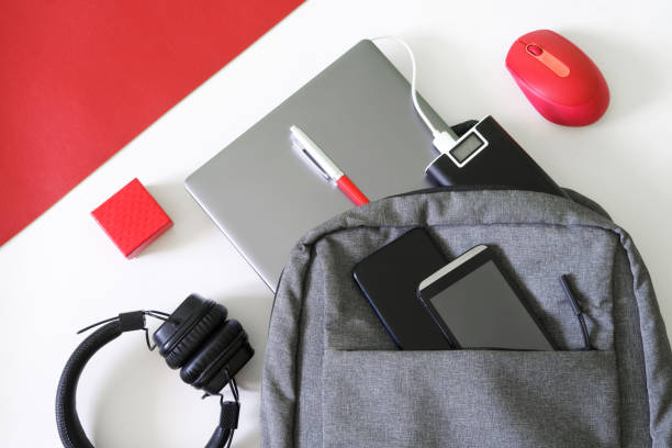 istock Gray backpack, laptop, two mobile smartphones, headphones, computer mouse, pen, red gift box and  power bank, on a white background. The concept of recharging devices while traveling 1403699386