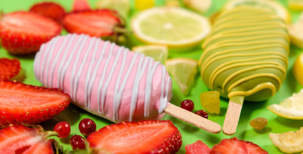 Two ice creams on a sticks - strawberry and lemon on a green background. Summer fruit desserts.