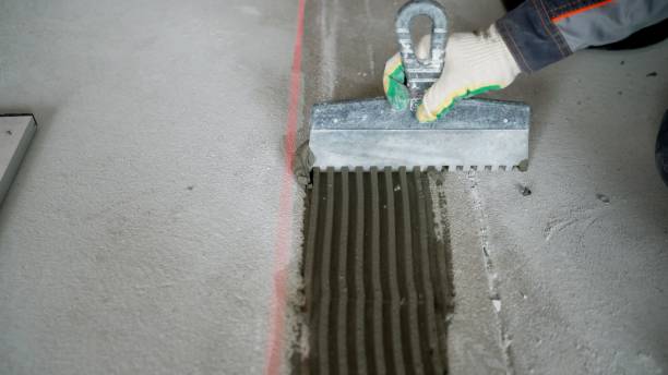 istock A professional worker erects a wall of blocks. The process of building a wall. Applying adhesive to a concrete floor with a spatula. 1403706264