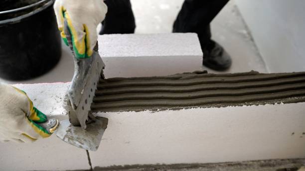 istock A builder lays aerated concrete blocks at a construction site. High-quality laying of blocks on glue, building a house. A worker glues blocks, builds a wall. 1403706294