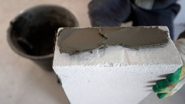 istock Block wall construction. A builder applies an adhesive mortar that uses lightweight concrete for construction. Applying glue to the block. 1403706469