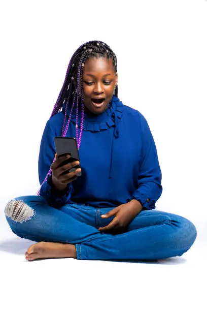A squatting female African Teenager looking into her smartphone with a surprised or shocked look