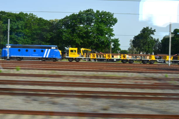 Vlaams-Brabant, Belgium - June 18, 2022: view from behind a windscreen in a moving train on Flemish landscapes. Stationary blue locomotive and yellow train carriage trailers. view on multiple railroad track junctions