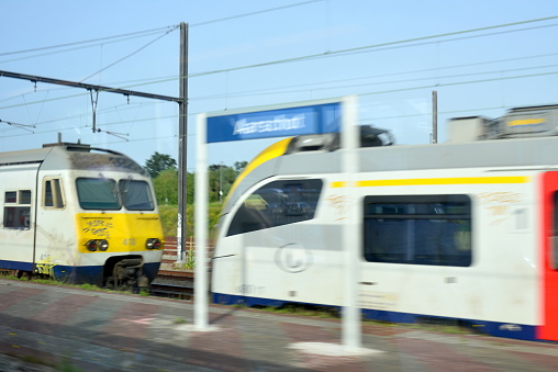 Aarschot, Vlaams-Brabant, Belgium - June 18, 2022: motion blur platform Aarschot railway station, view from behind a windscreen in a moving train, 2 trains one newer model, white locomotive with red passenger doors first class. In Belgium after the war the third class wooden benches for passengers was abolished staying with first and second class travel