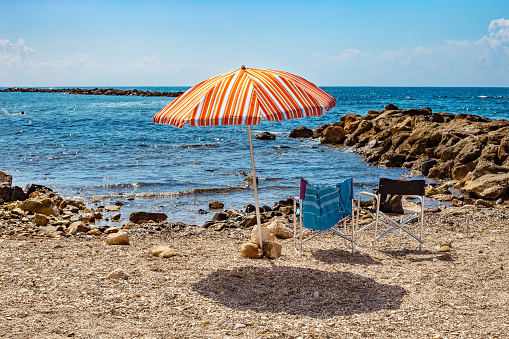 Sun umbrella and two chairs on a pebbly beach on sunny day at the blue sea background. Monterosso al Mare, Italy.