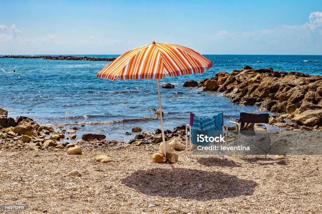 Sun umbrella and two chairs on a pebbly beach in Monterosso al Mare. Sun umbrella and two chairs on a pebbly beach on sunny day at the blue sea background. Monterosso al Mare, Italy. Italy Stock Photo