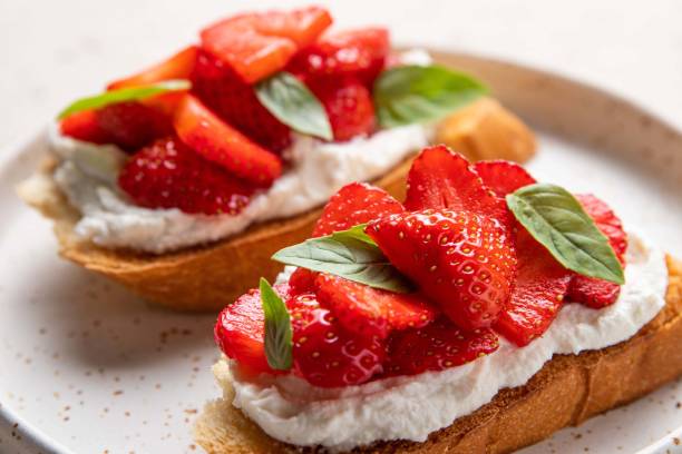 Homemade bruschettas with strawberries, cream cheese and basil in white plate on light background. Summer appetizer. Selective focus. Homemade bruschettas with strawberries, cream cheese and basil in white plate on light background. Summer appetizer. Selective focus. ricotta photos stock pictures, royalty-free photos & images