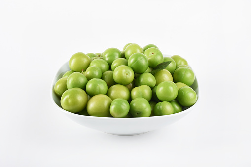 Group of green plums in the white bowl on the white background