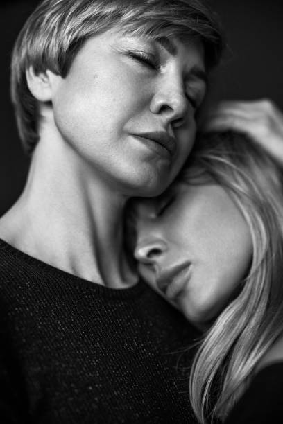 A man and woman are embracing each other in a park. The man is wearing a black shirt and the woman is wearing a white dress. Scene is romantic and intimate