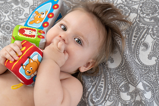 A baby with colorful cubes in his hands plays on the bed. Baby development concept, toddler restful sleep, teething, colic. View from above.