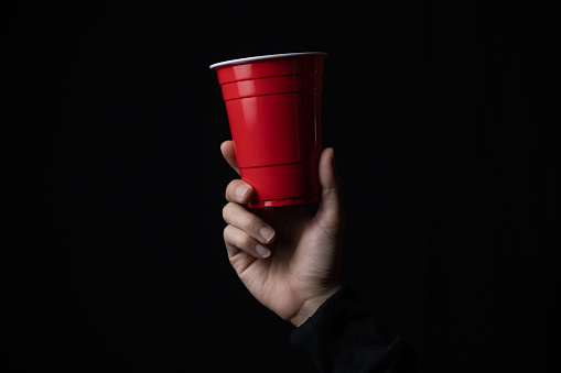 Red plastic cup with a hand in the dark, Close up.