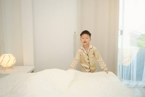 Little Asian boy child make up his room and fold the blanket in bedroom at home, Kid make the bed Happy little Asian kindergarten boy child make up his room and fold the blanket in bedroom at home, Kid make the bed, straightens a blanket on a large bed with good mood, Selective focus at the boy Independence in Daily Activities:  in kids stock pictures, royalty-free photos & images