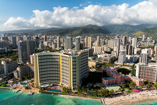 Aerial view of Waikiki Beach tall buildings by the beach in Honolulu, Hawaii. Blue sky with clouds above the mountains