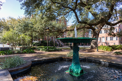 An old water fountain at Columbia Square park in the Historic District of Savannah Georgia with green trees