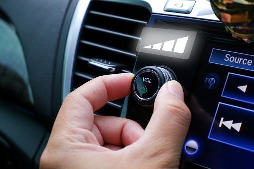 Driver hand adjust volume control on the car radio dashboard in the car