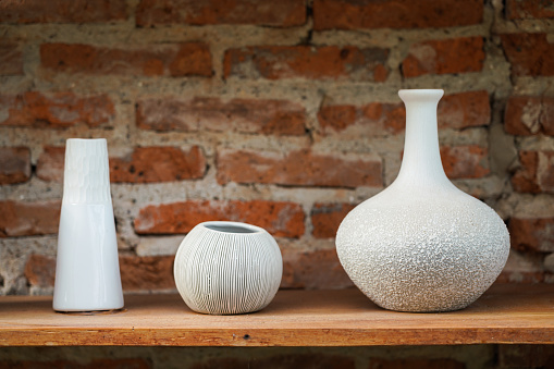 Set of crockery and ceramic kitchenware which is kept on the wooden shelf in red brick wall storage room. Interior object photo.