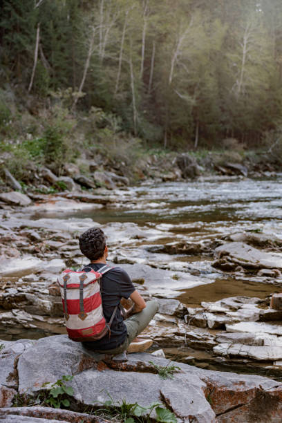istock Rear on man tourist with backpack sitting on rock at stream in mountains. Romantic view. 1403771370