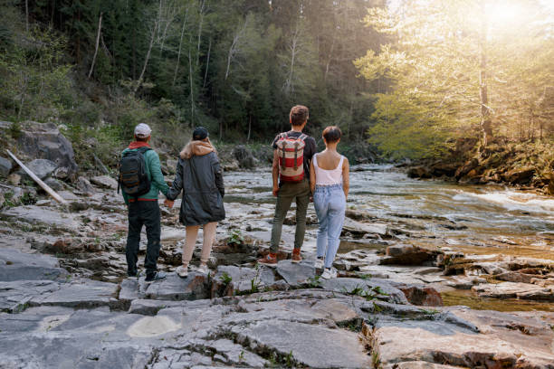 istock Rear on two couples standing hand in hand at river on rocks. Hikers in mountains valley. 1403771439