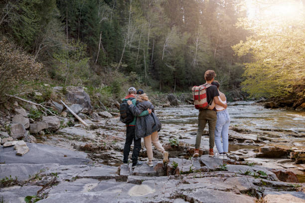istock Rear on two couples standing and hugging at river on rocks. Hikers in mountains valley. 1403771458