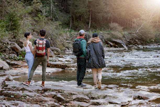 istock Back view on two couples at rocky fast mountains river standing hand in hand and enjoying view. 1403771473