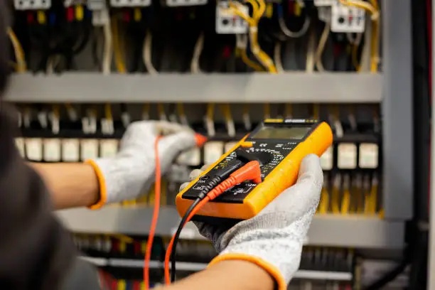 Photo of Electrician engineer uses a multimeter to test the electrical installation and power line current in an electrical system control cabinet.