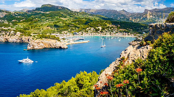 Panorama de la entrada al puerto de la marina Tramontana en Port de Sóller Mallorca en verano con montañas de la Serra de Tramuntana al fondo, playas de Sóller, barcos y flores en primer plano. photo