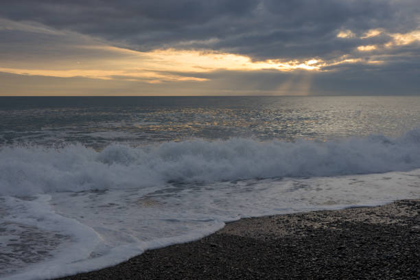 wellenförmiges meer bei sonnenuntergang, kieselstrand und wolken - cyclone stock-fotos und bilder