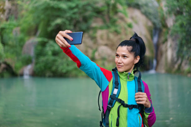 istock Smiling woman taking a selfie in front of a waterfall 1403784432