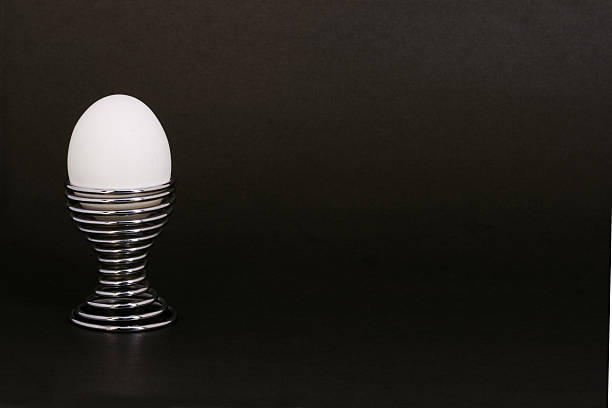 White egg in chrome eggcup on black background stock photo