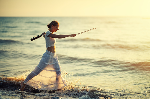 Happy teenage girl with a violin walking on the beach on sunset.\nCanon R5