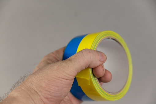 A man is holding yellow and blue duct tape in his hand. Reel of colored duct tape against the gray background. Selective focus. No people.