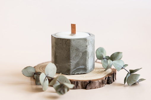 Handmade candles from paraffin and soy wax in concrete plaster candlestick with wooden wick and dry herbal isolated on pastel beige background. Copy space