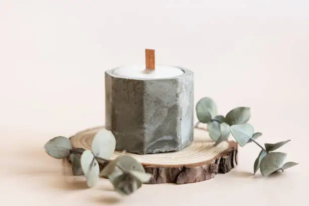 Photo of Handmade candles from paraffin and soy wax in concrete plaster candlestick with wooden wick and dry herbal isolated on pastel beige background. Copy space