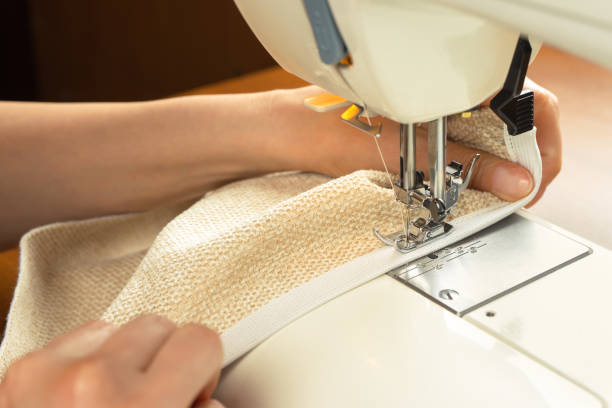 istock Female hands stitching white fabric on modern sewing machine. Close up view of sewing process. 1403795976