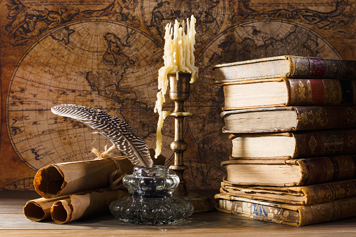 Vintage still life. Medieval table with candle near old books, scrolls, inkwell