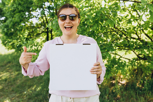 Young redhead woman in glasses holding box with pizza. Happy Girl pointing with hand and finger over street background. Delivery service concept. Fast pizza delivery. Mock up