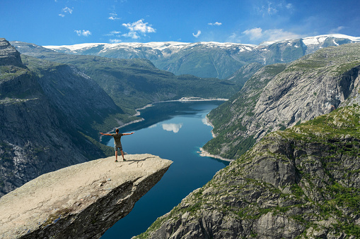 Norway - May 30, 2022: Trolltunga rock in summer with standing man. Ringedalsvatnet mountain lake - famous Norwegian hiking tourist landmark.