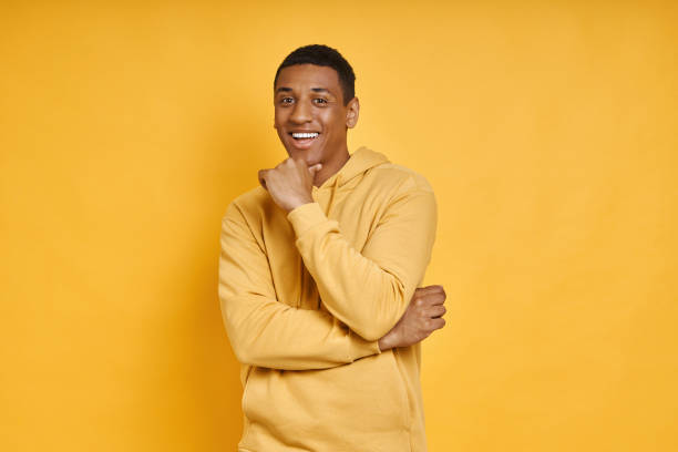 istock Cheerful mixed race man holding hand on chin while standing against yellow background 1403798825