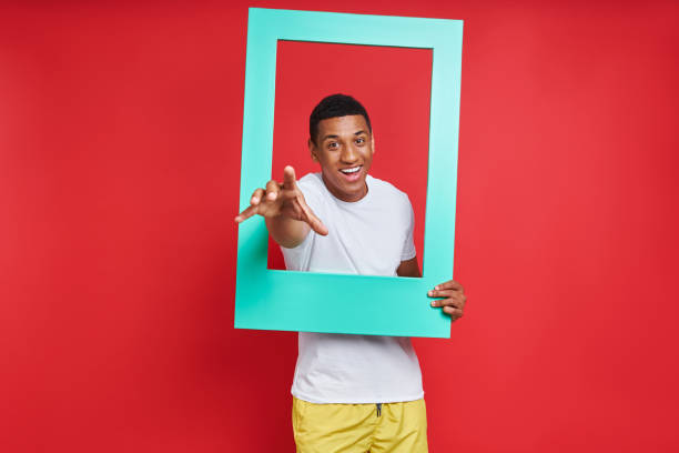 istock Playful mixed race man gesturing while looking through a picture frame against red background 1403798840