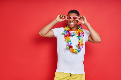 Happy young man in Hawaiian necklace standing against red background