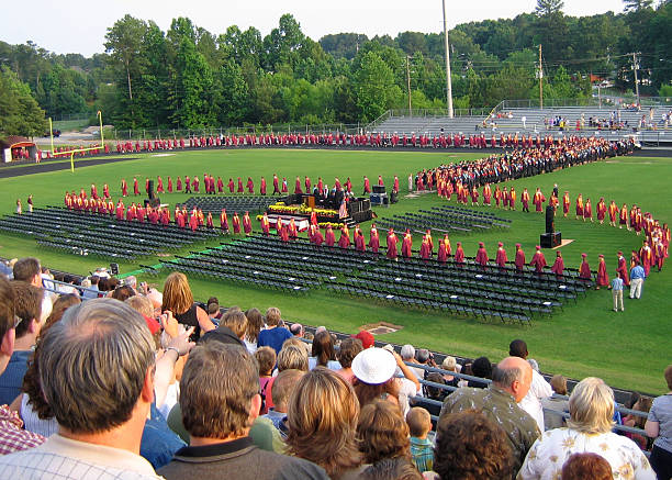 High School Graduation High school graduates file in their seats on the football field for the ceremony. school bleachers stock pictures, royalty-free photos & images