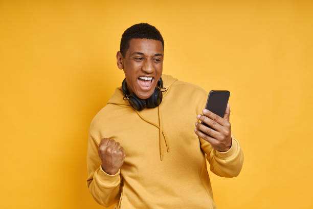 istock Excited mixed race man with headphones using smart phone 1403800586