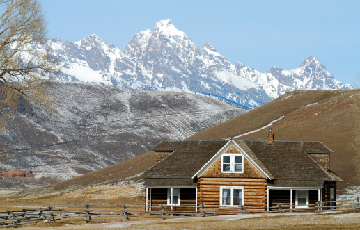 Log house on prarie with snow covered Gand Teton mountains in background