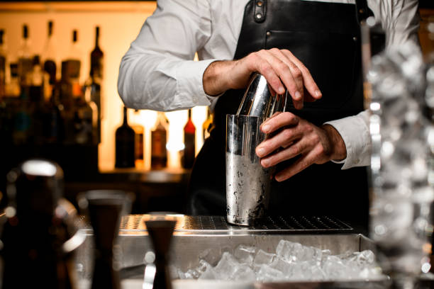 selective focus on shiny steel shaker on the bar counter, which is held by the hands of a male bartender stock photo