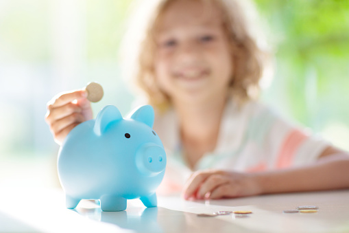 Child putting coin in piggy bank. Kids learn about money. Savings and investment. Little boy saving cash. Wealth growth for young family with children. Budget planning at home.