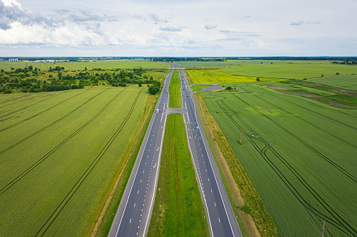 Asphalt highway through green summer field. Aerial view from drone