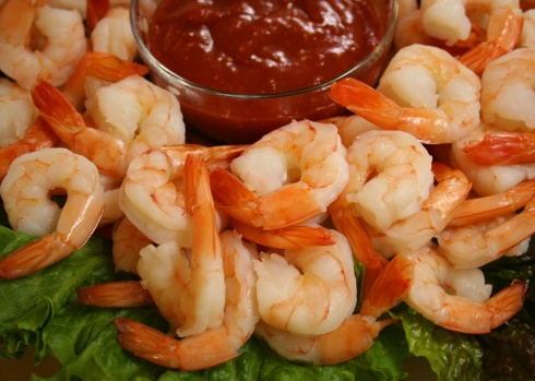 A pile of cooked shrimp on a platter with dipping sauce.