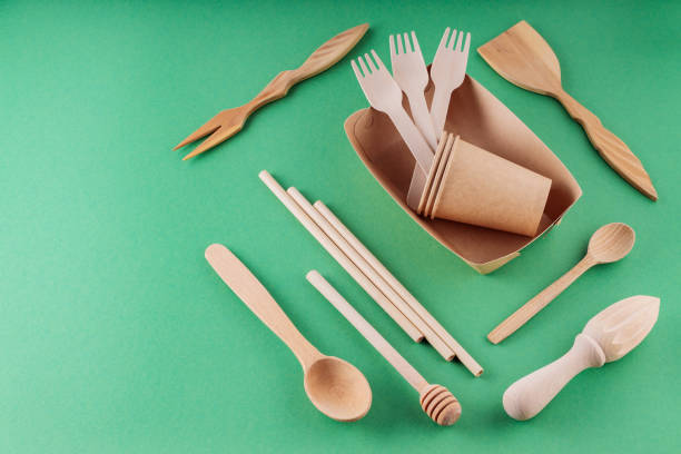 istock Paper biodegradable tableware and wooden cutlery on a green background. Eco-friendly kitchen utensils, bamboo forks, cardboard containers and cups. Sustainable lifestyle. Copy space 1403809370
