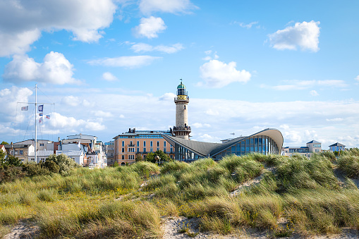 WARNEMUENDE (ROSTOCK), MECKLENBURG-WEST POMERANIA, GERMANY – AUGUST 02 2021: The lighthouse and landmark Teepott with the skyline of Warnemuende in Germany photographed from the dunes.